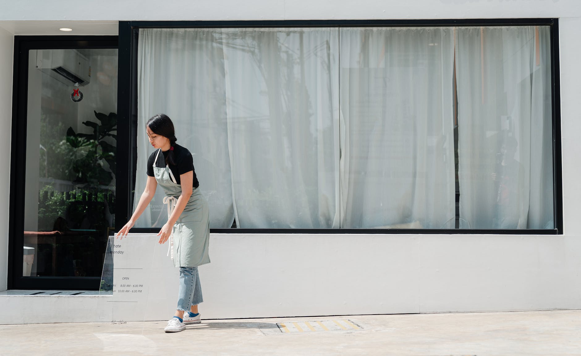 young female employee in uniform placing signboard against cafe